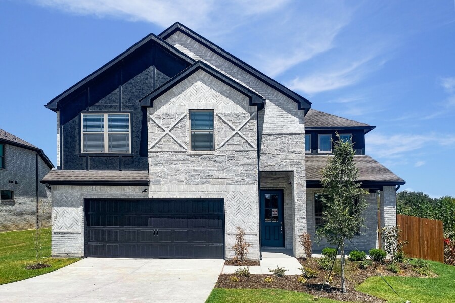 Modern two-story home with stone facade and black garage door under a clear sky.