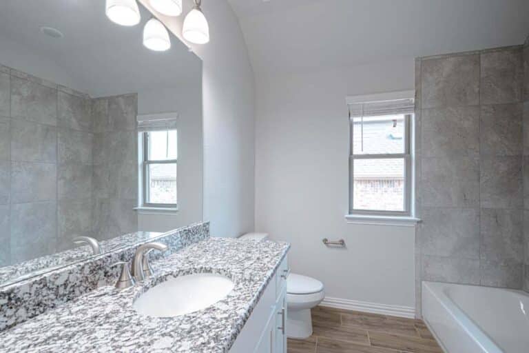 Modern bathroom with granite countertop, dual sinks, and gray tile.