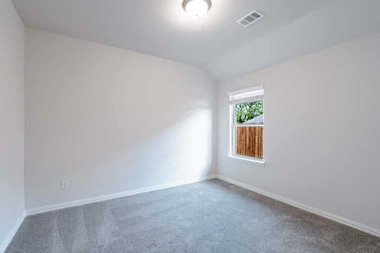 An empty room with white walls, carpet flooring, and a single window.
