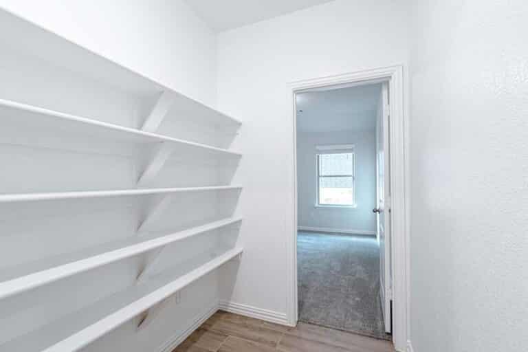 Empty white shelves in a clean, bright room with an open door leading to another room.