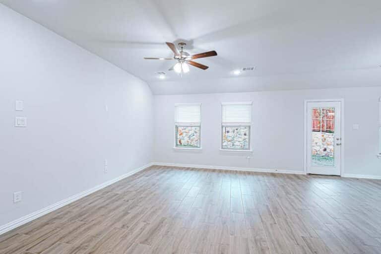 Empty room with hardwood floors, ceiling fan, and two windows.