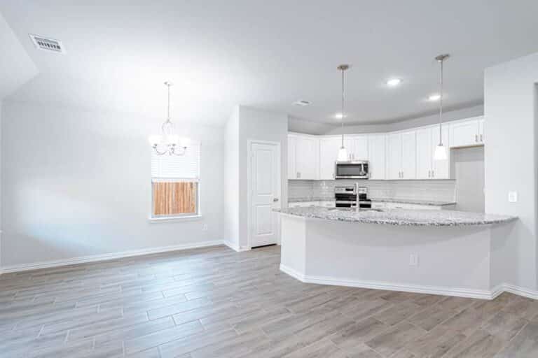 Modern kitchen with white cabinetry and stainless steel appliances, featuring an island countertop and hardwood floors.