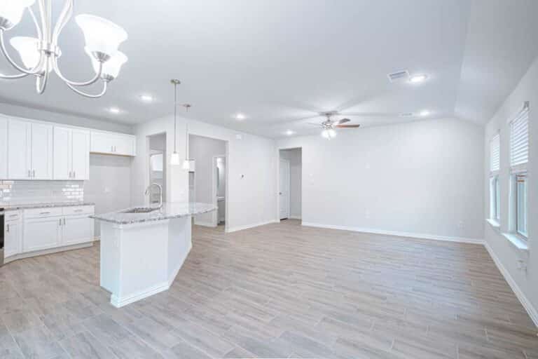 Bright, spacious kitchen with white cabinets and modern appliances, featuring a central island and wooden flooring.