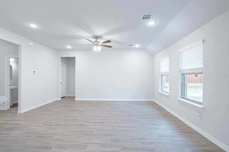 Empty, bright living room with tiled flooring and ceiling fan.