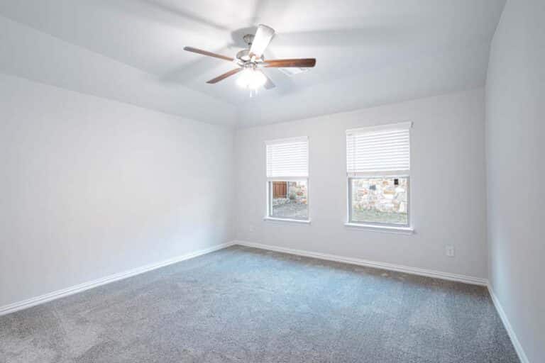 An empty room with white walls, two windows, and a ceiling fan.