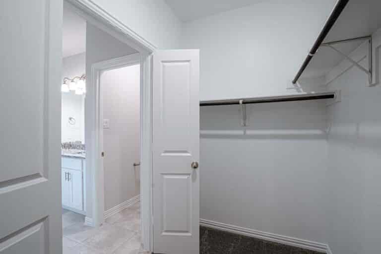 An empty walk-in closet with an open door leading to a bathroom.