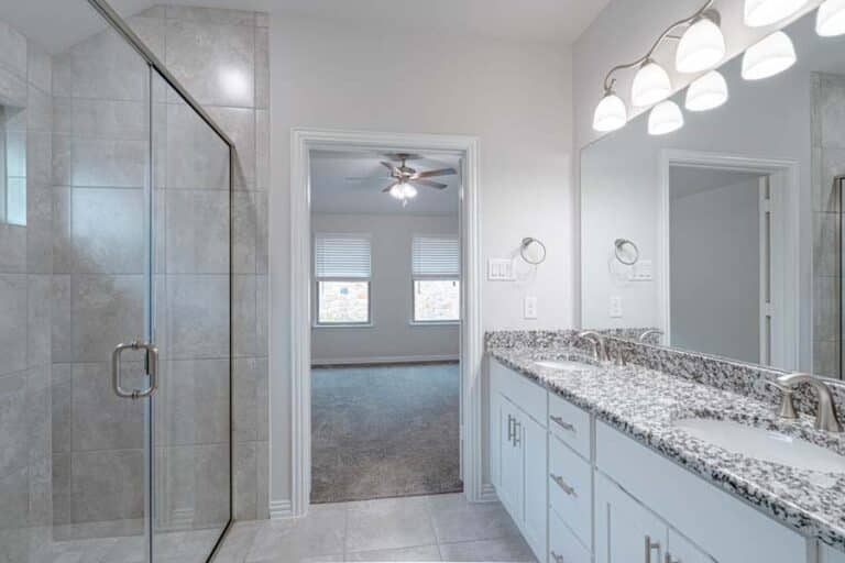 Modern bathroom interior with dual sinks, granite countertops, and a glass shower enclosure.