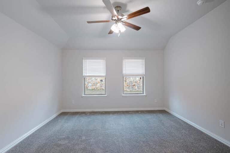 Empty room with carpet flooring, two windows, and a ceiling fan.