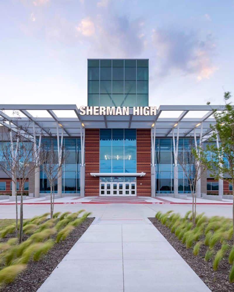 Modern high school entrance with landscaped pathway at dusk.